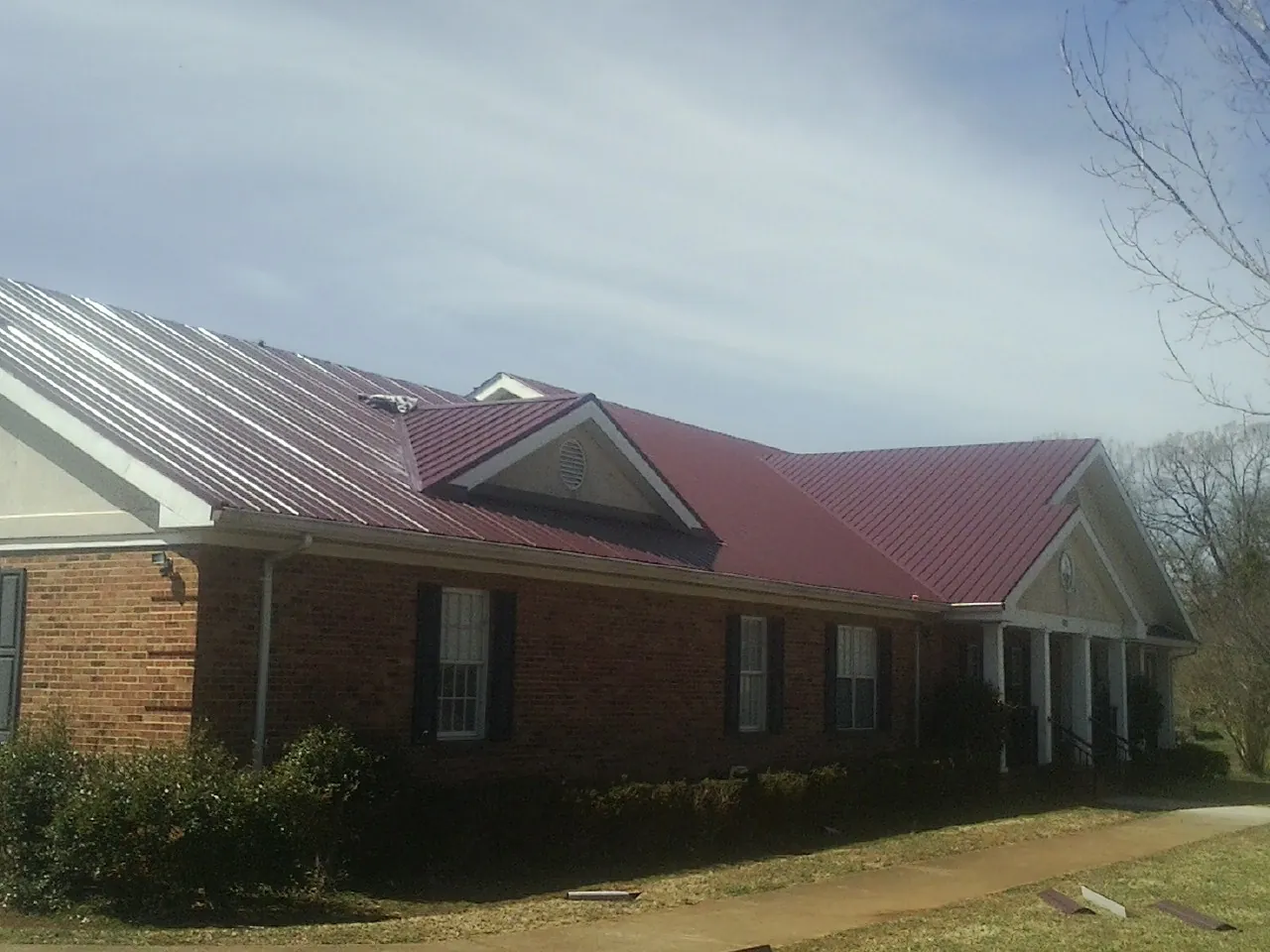 Red metal roof with gabled entries on a long brick building, from a Hail Damage Roof Repair job in Twin Falls