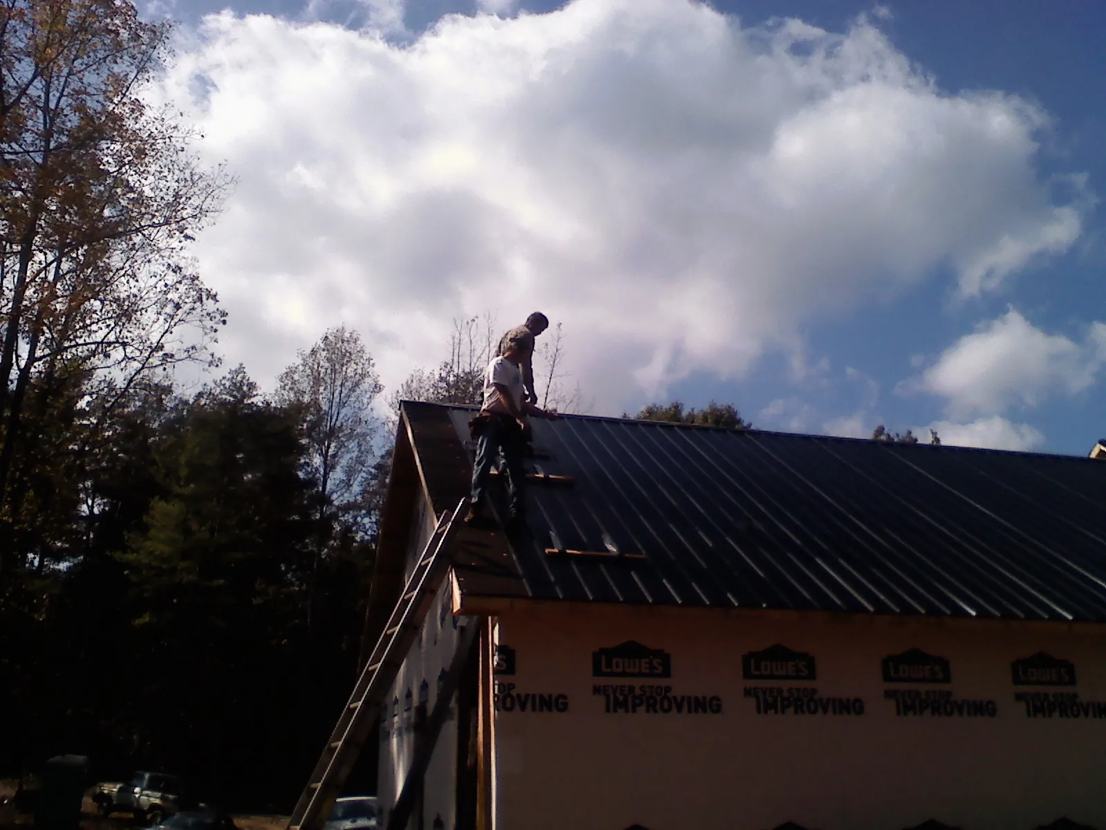 Roofer fastening dark metal panels high against a cloudy sky, from a Roof Inspection job in Twin Falls