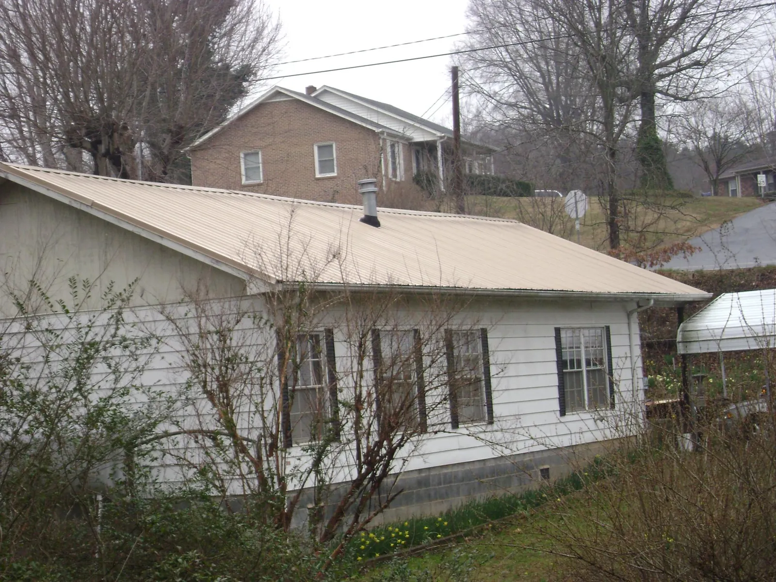 Tan metal roof on a white sided house set into a hillside — Commercial Roofing by Roofing Brothers in Twin Falls